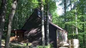 Une cabane au revêtement extérieur en bois, entourée d’arbres. Elle est dotée d’une véranda avec une balustrade et d’une table de pique-nique.