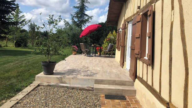 Une terrasse avec un parasol rouge, des plantes en pot et une table en bois.