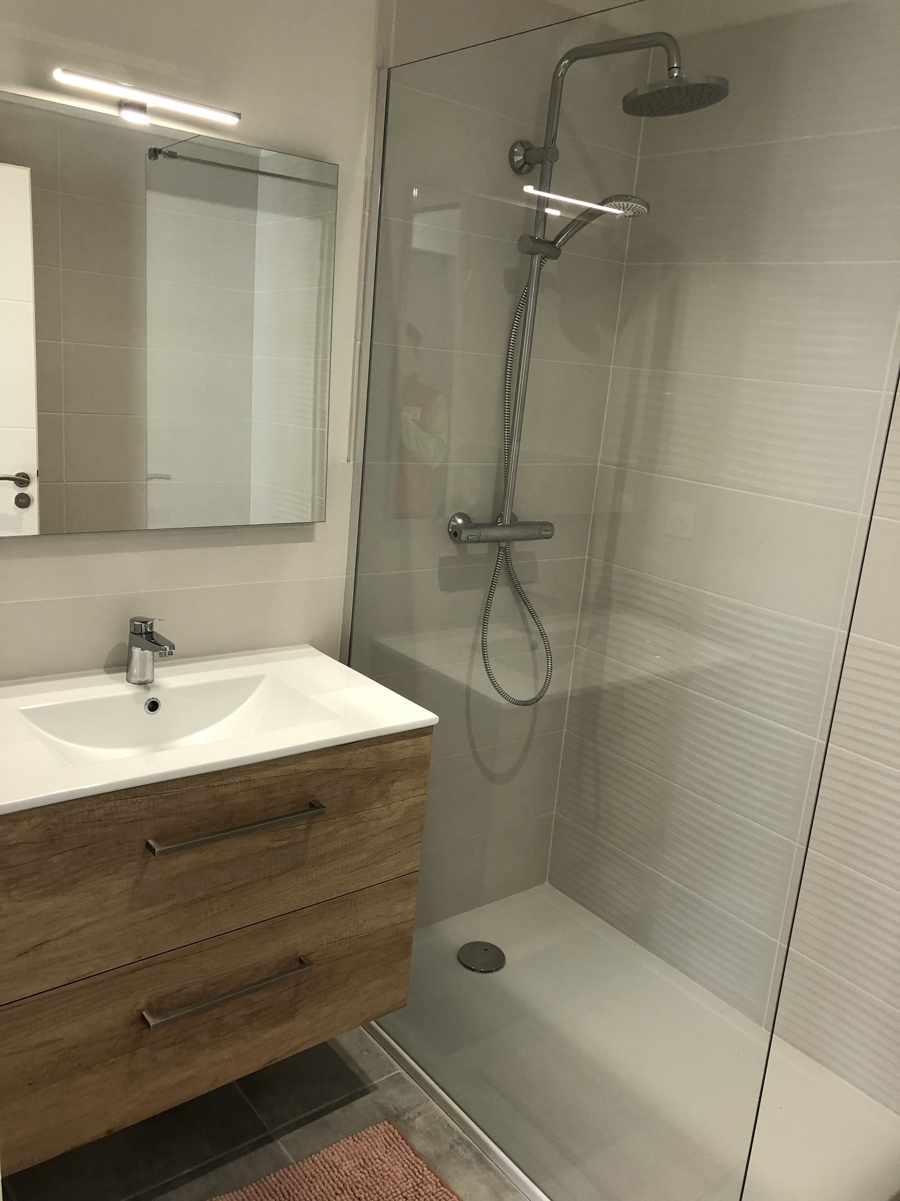 A modern bathroom with a white sink, wooden vanity, and a glass shower enclosure.