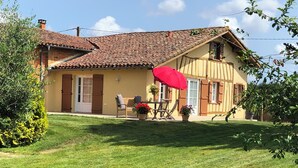 Une maison avec un toit en tuiles, une porte d’entrée et une terrasse avec une table et des chaises.