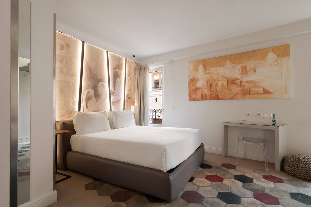 A modern bedroom with a large bed, a desk, and a painting on the wall.