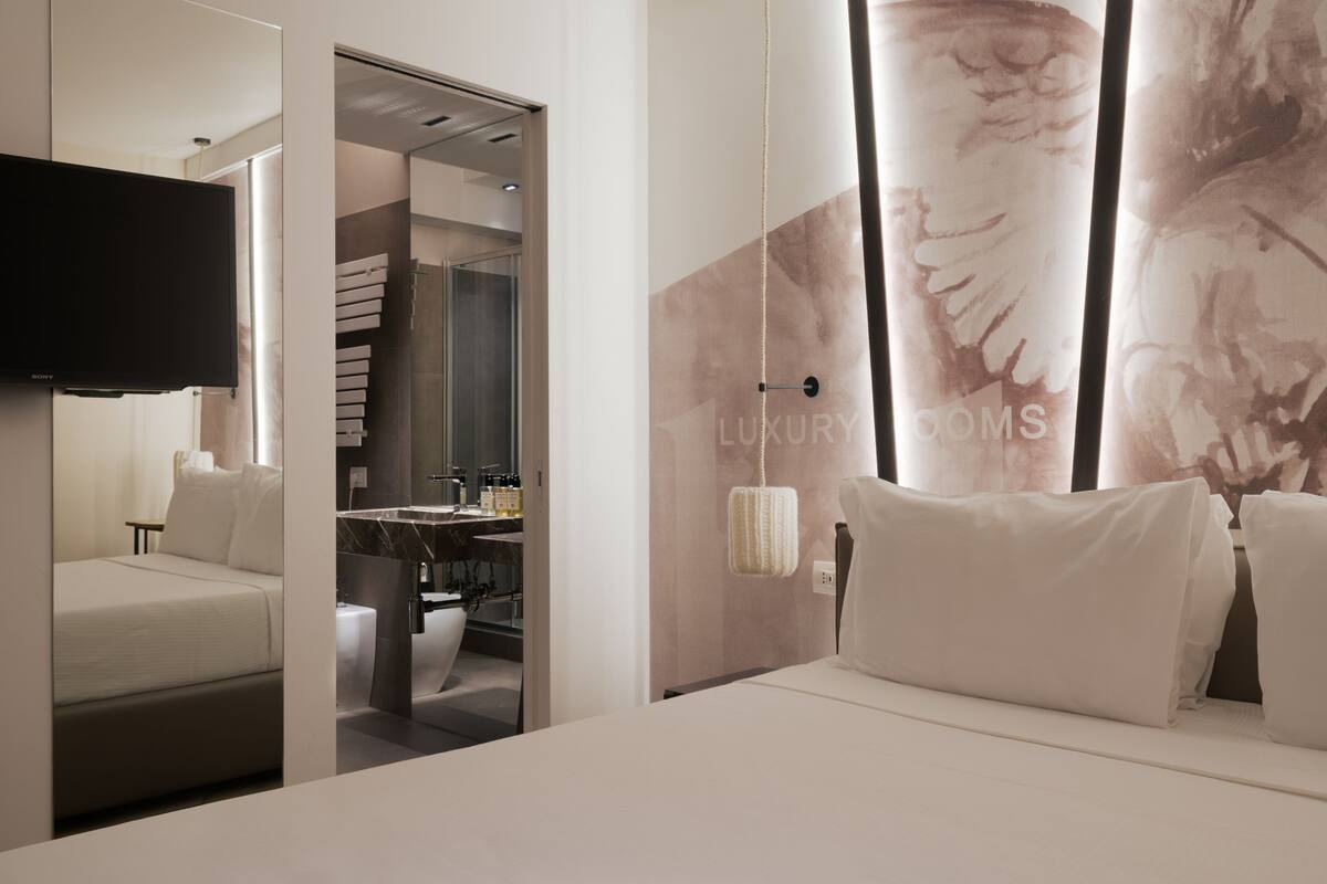 A modern hotel room with a bed, a TV, a bathroom, and a large mirror.