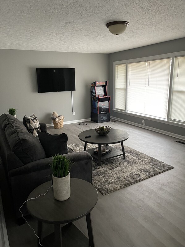 A living room with a sofa, coffee table, and a TV mounted on the wall. - Red Door On Riverview (Bowling Green)