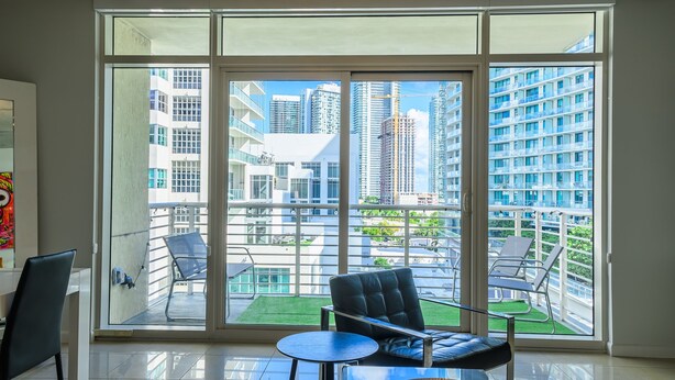 Quarto moderno com grandes portas de vidro deslizantes que dão para uma varanda com mobiliário externo.