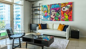 Uma sala de estar moderna com um sofá branco, uma mesa de centro preta e obras de arte coloridas na parede.