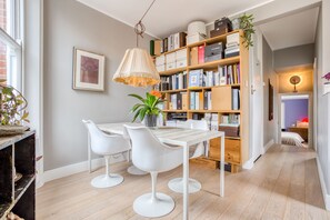 Een eethoek met een tafel, stoelen, een boekenkast en een hanglamp.