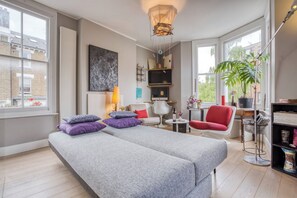 Un salon moderne comprenant un canapé, des fauteuils, une table basse, un téléviseur et une bibliothèque.