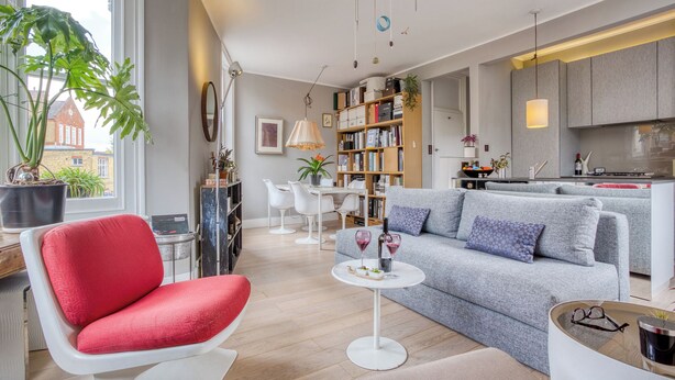 Una sala de estar moderna con un sillón rojo, un sofá gris y una pequeña mesa redonda con copas de vino.