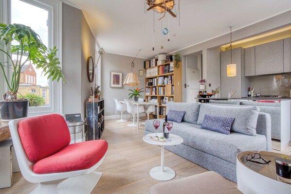 A modern living room with a red chair, grey sofa, and a small round table with wine glasses.