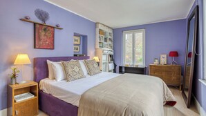 Un dormitorio con cama, mesitas de noche, cómoda, estantería y ventana.