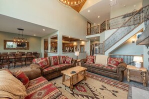 A spacious living area with a high ceiling, a staircase, and a dining area with wooden furniture.