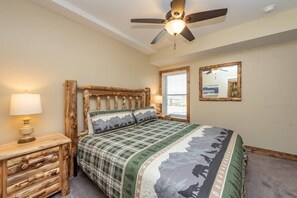 A bedroom with a wooden headboard, a bed with a mountain-themed bedspread, a nightstand with a lamp, a ceiling fan, and a window with blinds. - Lazy Creek - Deep Creek Lake - Indoor Lazy River , Boat Dock rental available May-Sept. 2026 (Deep Creek)