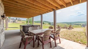 An outdoor patio with a wooden table and chairs, a hot tub, and a view of the countryside.