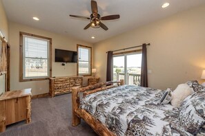 A bedroom with a large bed, wooden headboard, a ceiling fan, a flat-screen TV, and a window with blinds. - Lazy Creek - Deep Creek Lake - Indoor Lazy River , Boat Dock rental available May-Sept. 2026 (Deep Creek)