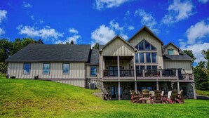 A large, two-story house with a stone foundation, multiple windows, and a balcony with outdoor furniture.