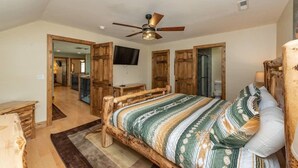 A bedroom with a wooden bed frame, a ceiling fan, and a television on the wall.