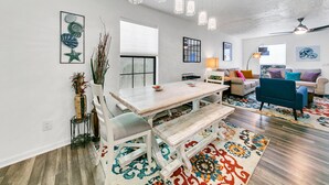Uma sala de estar moderna com uma mesa de jantar de madeira, cadeiras brancas, um sofá azul e um tapete colorido.