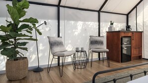 A modern room with a large plant, two chairs, a small table, a cabinet, and a ceiling fan. - Cherry Cove Glamping W/ Hot tub AND Cowboy Pool! (Fredericksburg)