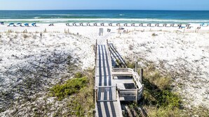 Une plage avec une promenade en bois menant à l’eau, bordée de parasols et de chaises de plage.