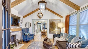 A spacious living room with a high ceiling, wooden beams, a fireplace, a blue armchair, a brown sofa, and a dining area in the background. - Completely Renovated Historical Cottage -- Walking distance to Downtown Franklin (Franklin)