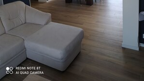 Ein modernes Wohnzimmer mit einem weißen Sofa, einem Essbereich mit Tisch für vier Personen und Blick auf einen Swimmingpool.