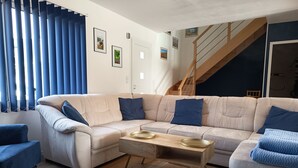 Ein Wohnzimmer mit einem beigefarbenen Ecksofa, einem Holztisch und einer Treppe, die in einen oberen Bereich führt.