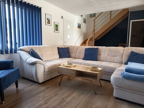 Una sala de estar con un sofá seccional color beige, una mesa de centro de madera y una escalera que sube a un nivel superior.