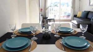 A dining table set with blue plates, clear glasses, and silverware, with a view of a balcony and a sofa in the background. - 2 Bed 2 Bath Beautiful Apt Next to Villamartin Plaza (Orihuela Costa)