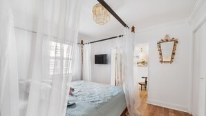 A bedroom with a four-poster bed, a chandelier, a flat-screen TV, and a mirror on the wall.