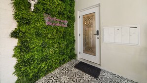 A white door with a decorative glass panel, a wall covered in green foliage, a white wall, and a black doormat.