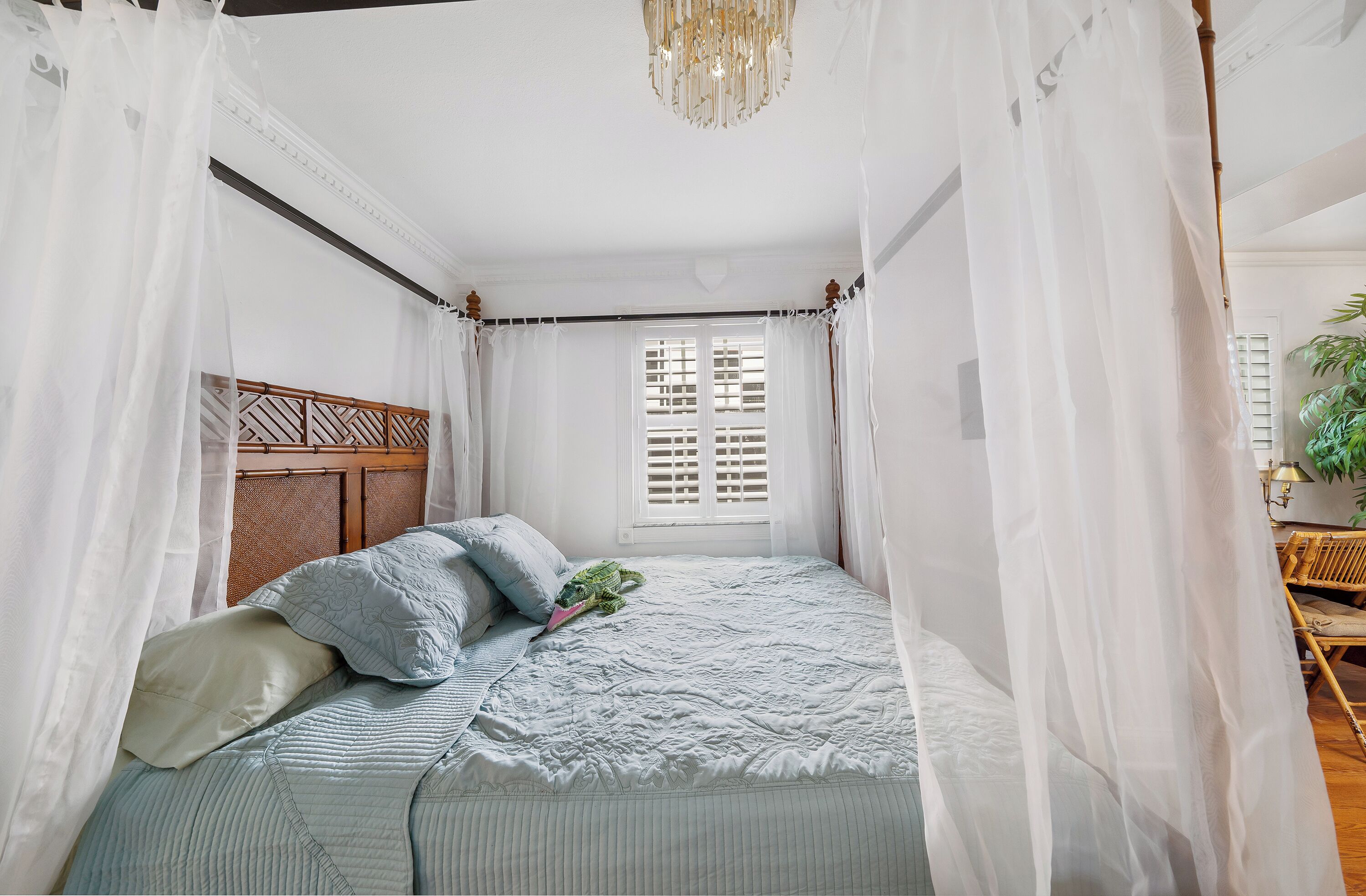 Een slaapkamer met een hemelbed, een raam met luiken, en een houten hoofdbord.