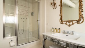 Een moderne badkamer met een douchecabine van glas, een witte wastafel met spiegel met gouden rand, en netjes opgevouwen handdoeken.