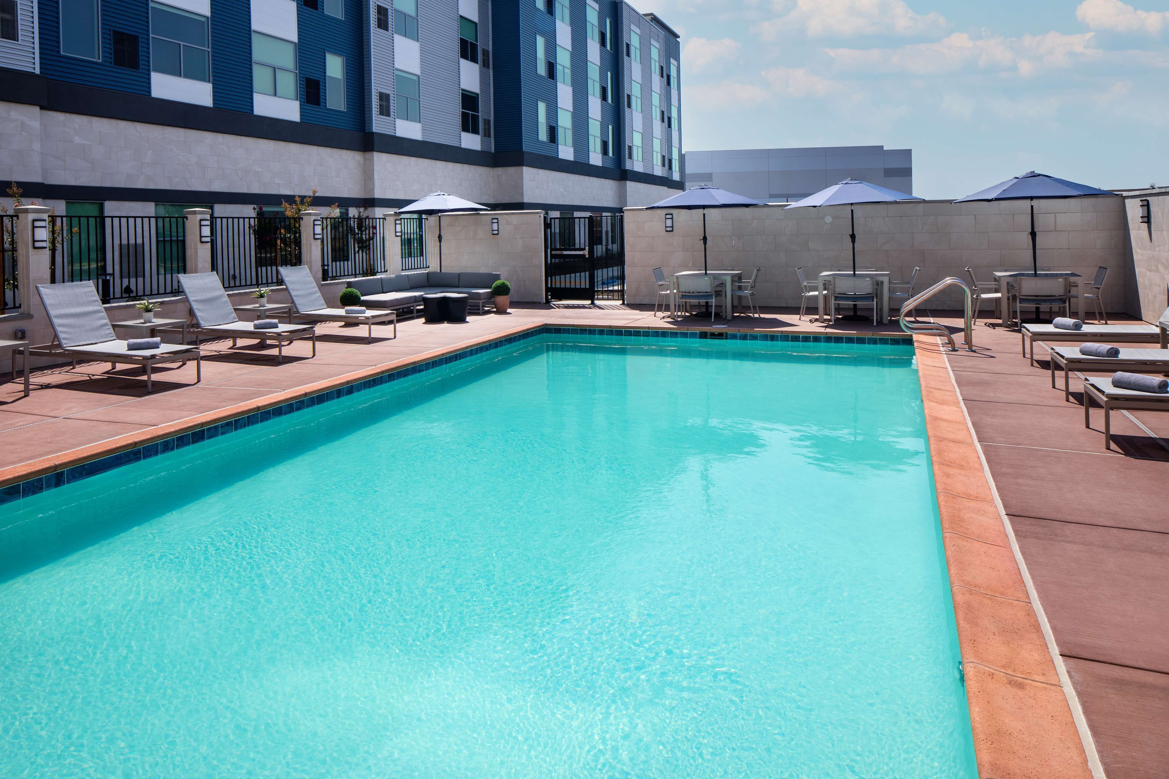 Una piscina con sillones de descanso y sombrillas, rodeada por un edificio de diseño moderno.