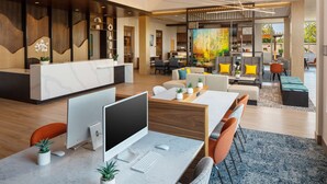 Un espace de bureau moderne comprenant un comptoir d’accueil, des postes de travail équipés d’ordinateurs et un coin repas agrémenté d’un grand tableau.