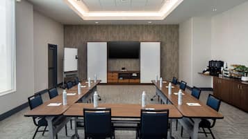 Una sala de conferencias con una mesa larga, sillas, un televisor de pantalla plana y una estación de café.
