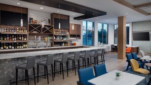 Un espace bar moderne doté d’un long comptoir, de nombreux tabourets et d’une grande variété de bouteilles et de verres.