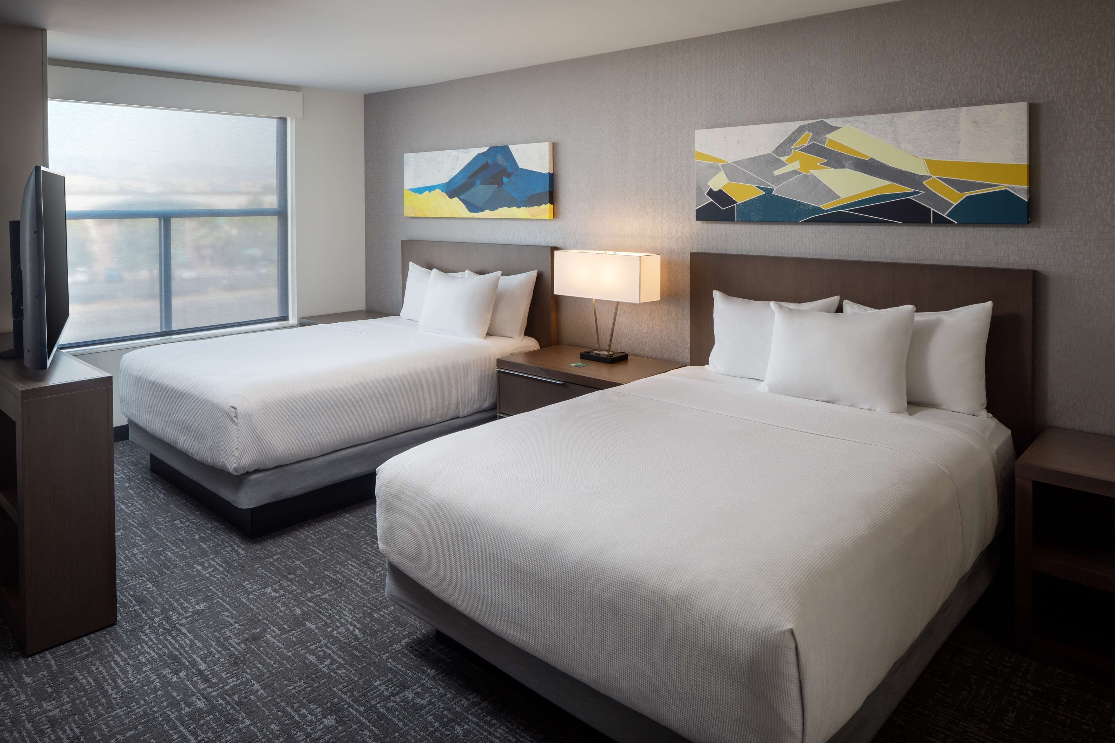 A hotel room with two beds, a TV, and artwork on the walls.