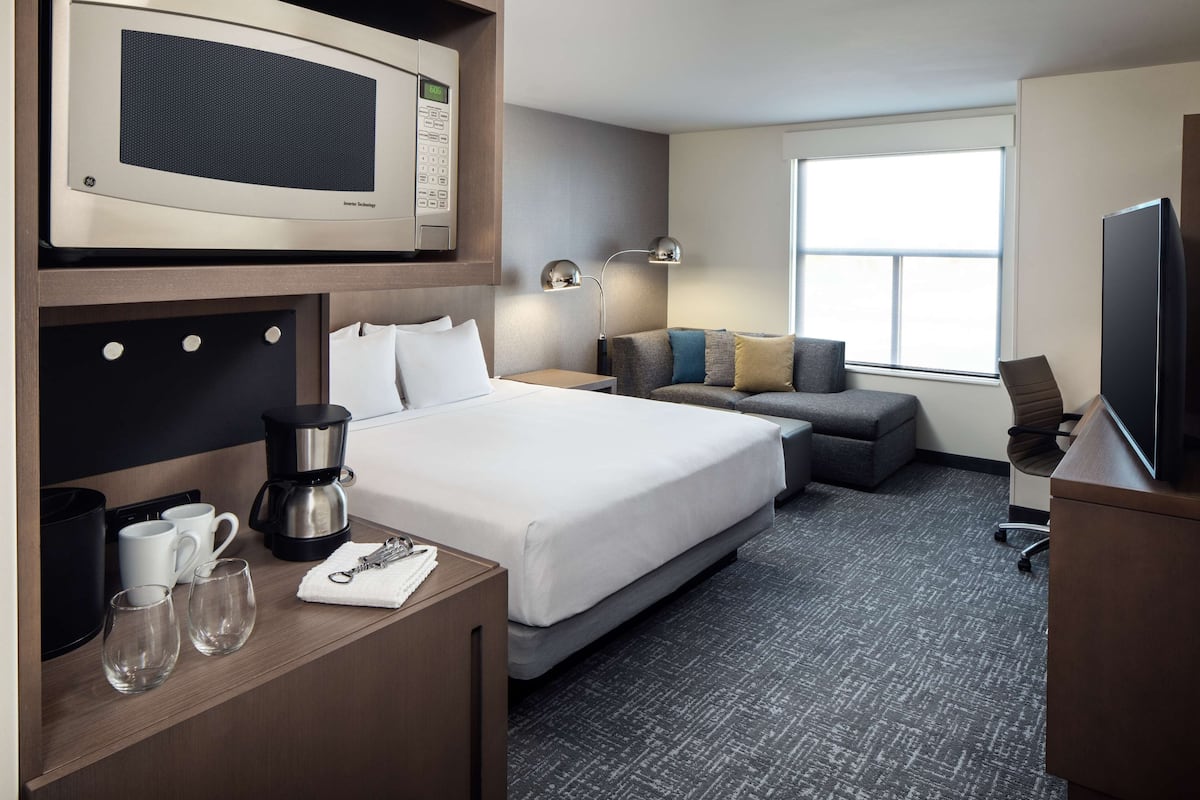 Een hotelkamer met een bed, een bureau met een koffiezetapparaat, een magnetron, een televisie en een raam met natuurlijk licht.
