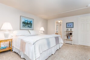 A bedroom with a large bed, two bedside lamps, a bedside table with a lamp, a bookshelf, and a door leading to another room. - Salmon Run Vacation Rental! (Ketchikan)