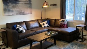 Ein modernes Wohnzimmer mit einem braunen Ledersofa, einem Holztisch und einem Teppich in Blau und Weiß.