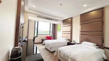 A hotel room with two beds, a desk, a chair, a TV, and a window with a view.