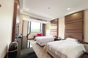 Habitación de hotel con dos camas, un escritorio, una silla, un televisor y ventana con vistas.
