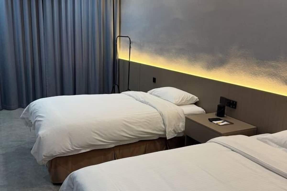 Habitación de hotel con dos camas, una mesita de noche, una lámpara y vistas al cielo.