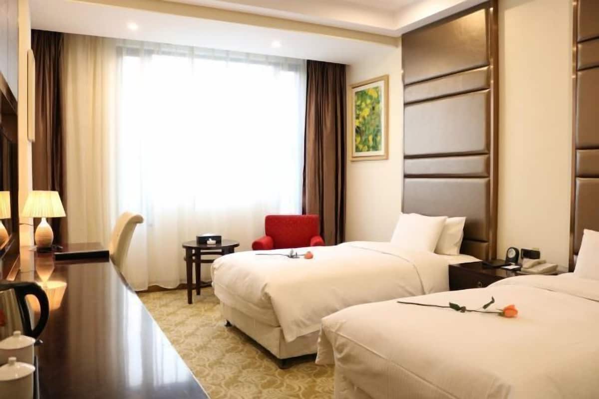 Una habitación de hotel con dos camas, un escritorio con lámpara, una mesita pequeña y una silla roja.