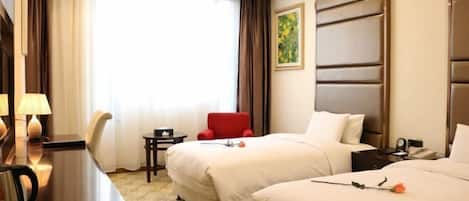 A hotel room with two beds, a desk with a lamp, a small table, and a red chair.