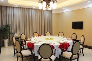 Un salón de conferencias con una mesa redonda, sillas, una araña, una televisión y un telón de fondo.