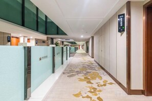 Un pasillo de hotel con piso alfombrado, divisiones de vidrio y un letrero que indica la dirección al ascensor.