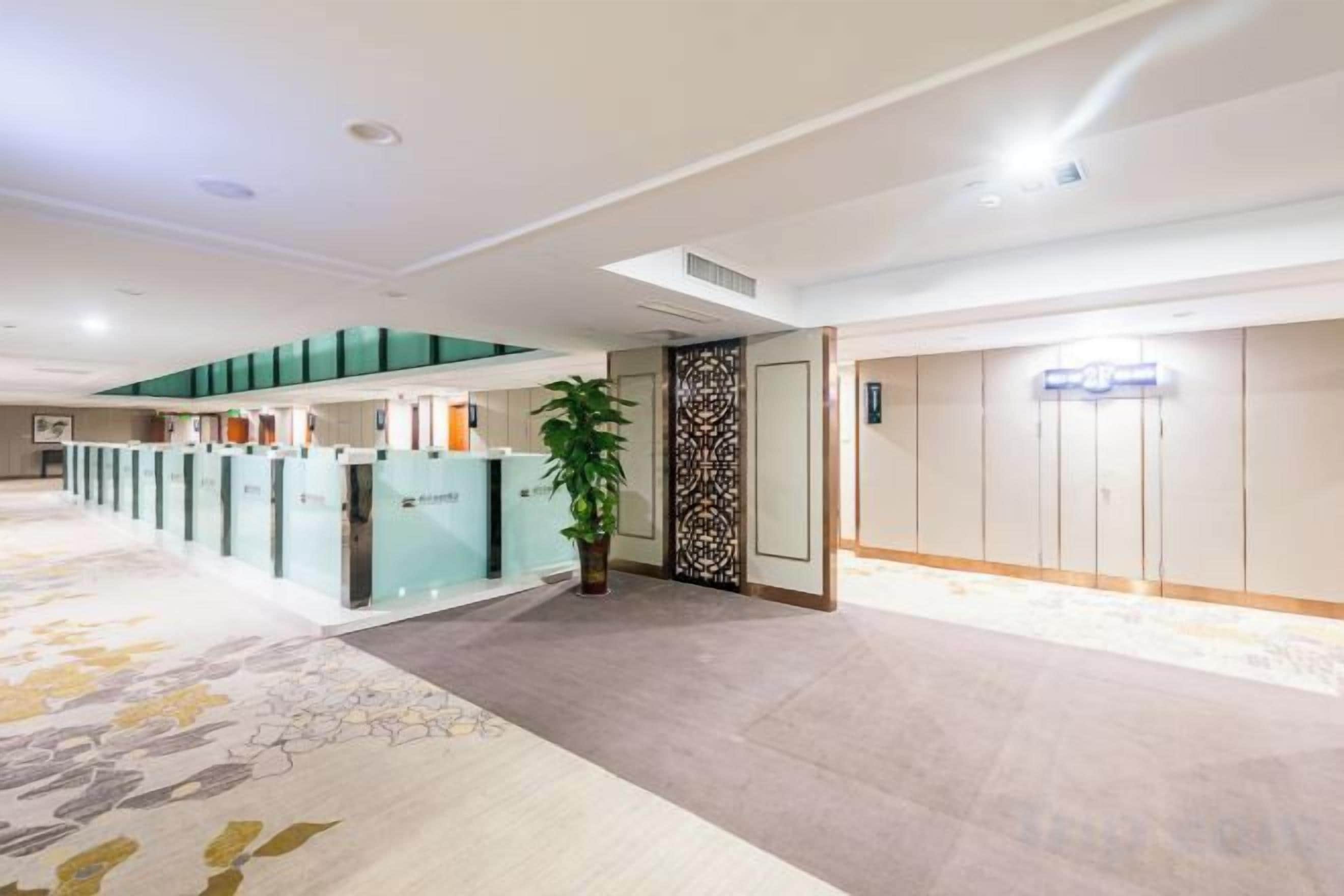 A hotel reception area with a reception desk, a potted plant, and a wall-mounted elevator.