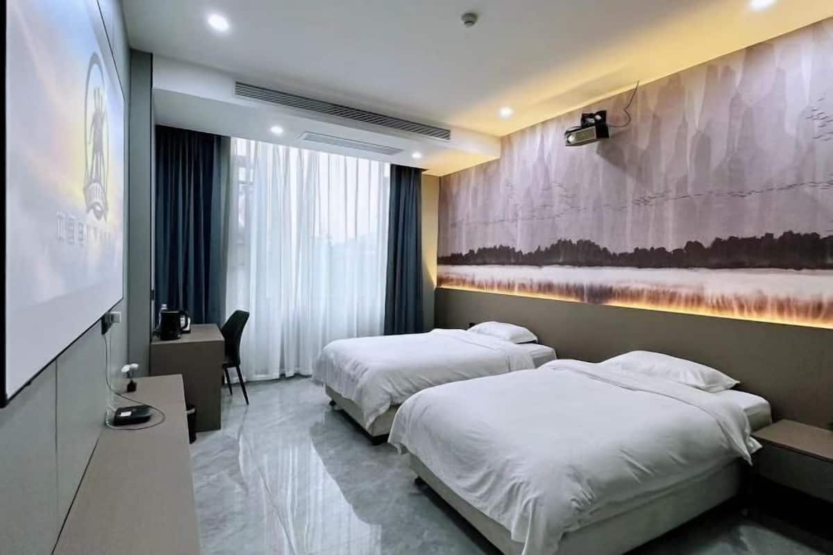 Habitación de hotel con dos camas, un escritorio, una silla, una pantalla de proyector y un mural grande en la pared.