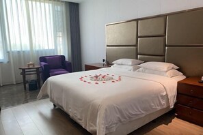 Une chambre d  ’hôtel avec un grand lit, une table de chevet en bois, un fauteuil violet et une petite table avec une lampe.